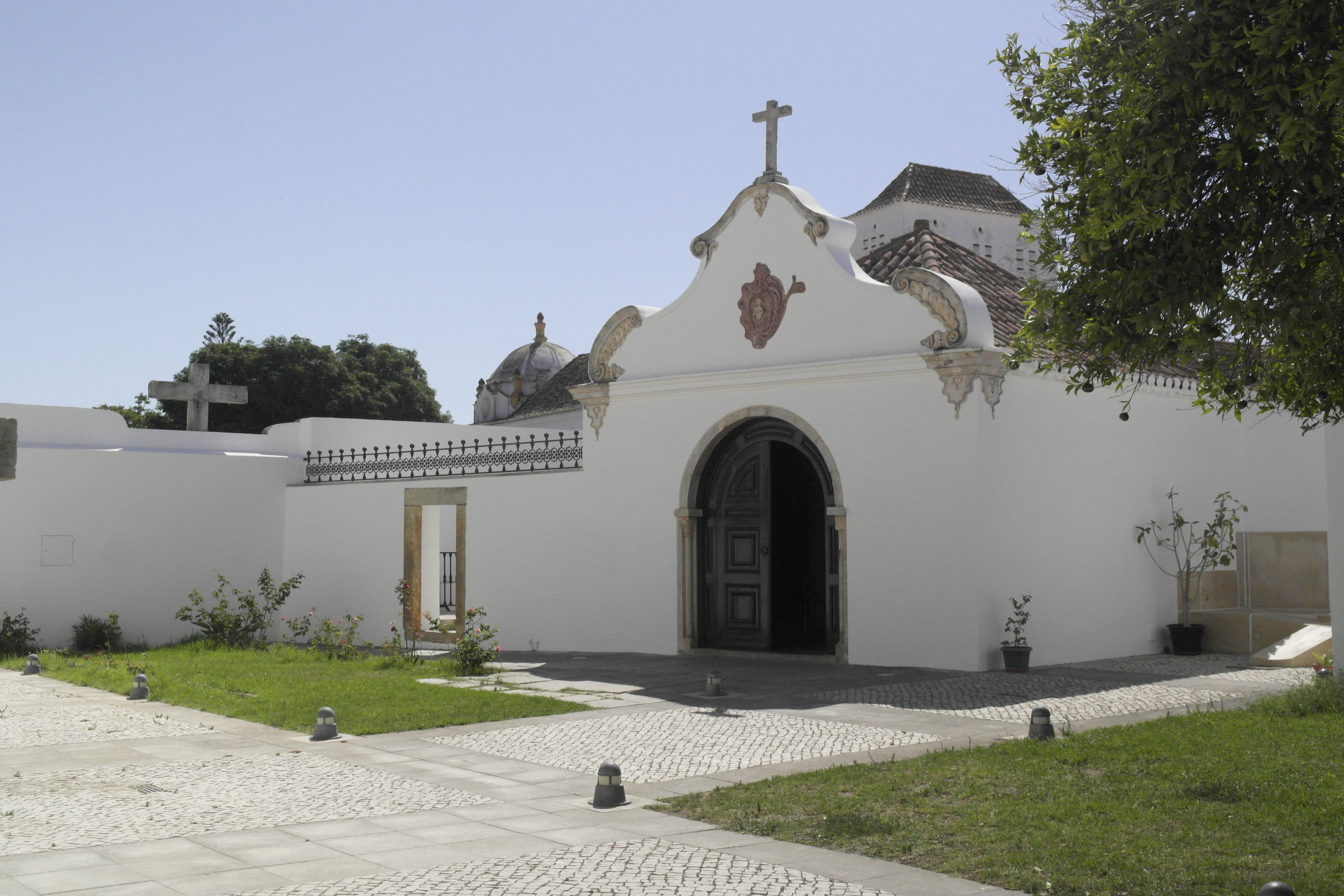 Entrée de chapelle blanche, croix au-dessus du fronton arrondi, petit jardin devant